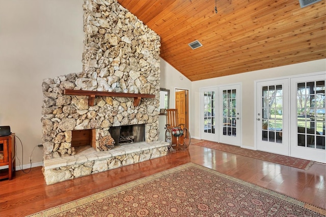 unfurnished living room with hardwood / wood-style floors, high vaulted ceiling, a stone fireplace, and french doors