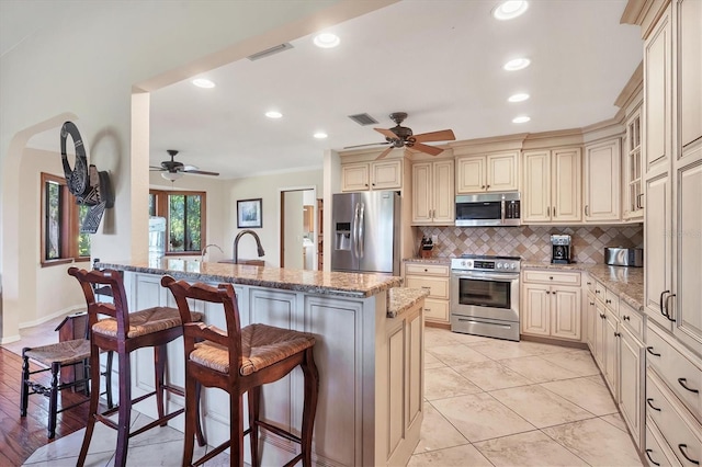 kitchen featuring light stone countertops, appliances with stainless steel finishes, ceiling fan, and a breakfast bar area