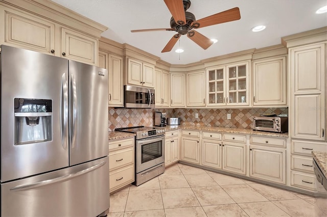 kitchen with appliances with stainless steel finishes, backsplash, light stone counters, and cream cabinets