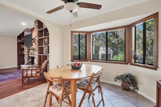 tiled dining space with built in shelves, ceiling fan, a stone fireplace, and vaulted ceiling