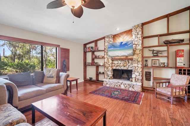 living room with hardwood / wood-style flooring, ceiling fan, a stone fireplace, and lofted ceiling