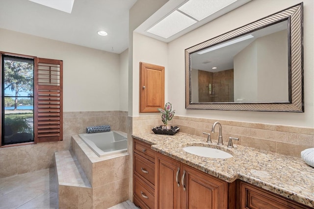 bathroom featuring a skylight, vanity, and a relaxing tiled tub