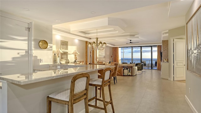 kitchen featuring light stone countertops, a kitchen bar, kitchen peninsula, ceiling fan with notable chandelier, and a water view