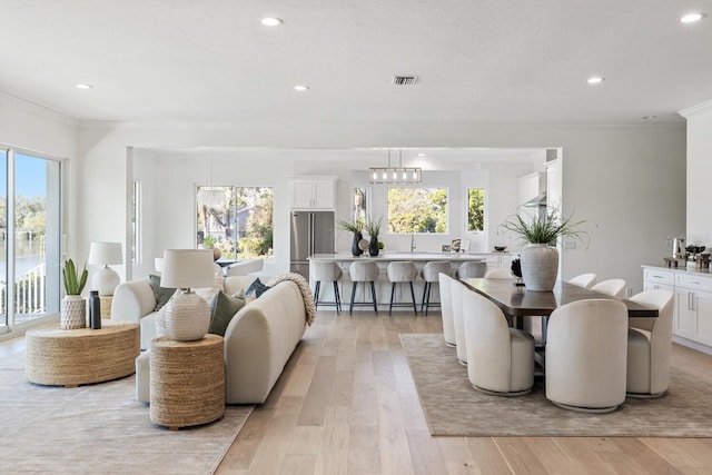 dining space with a chandelier, light hardwood / wood-style floors, crown molding, and a healthy amount of sunlight