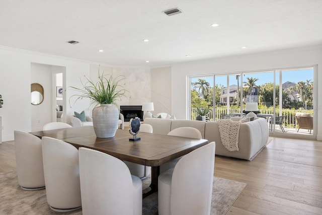 dining area with light hardwood / wood-style floors, ornamental molding, and a high end fireplace