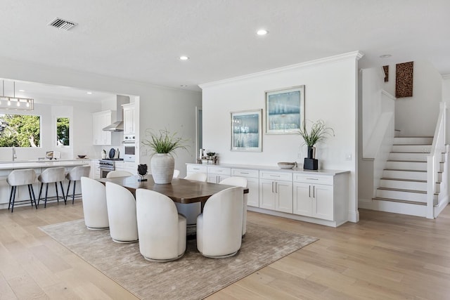 dining room with light wood-type flooring, ornamental molding, and sink