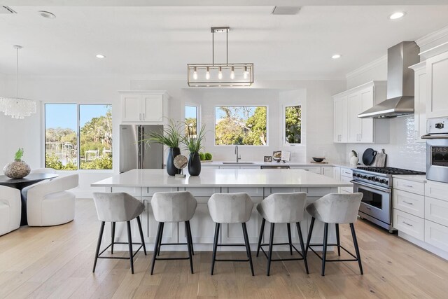 kitchen with wall chimney exhaust hood, premium appliances, a kitchen island, and decorative light fixtures