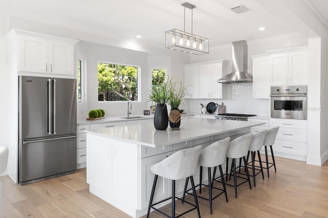 kitchen featuring a center island, white cabinets, stainless steel appliances, and wall chimney range hood