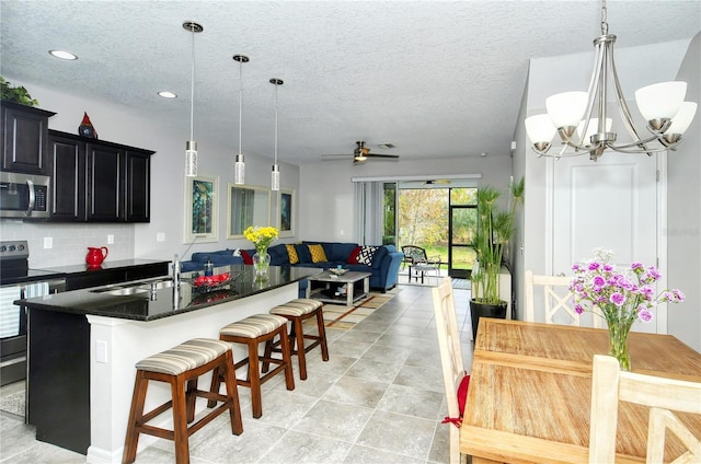 kitchen featuring stainless steel appliances, pendant lighting, a kitchen bar, a center island with sink, and ceiling fan with notable chandelier