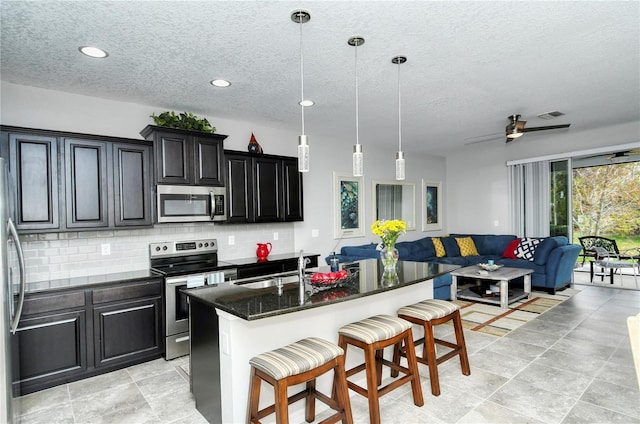 kitchen featuring a center island with sink, sink, a breakfast bar area, decorative light fixtures, and stainless steel appliances