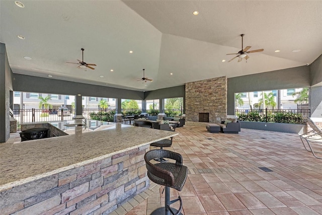 view of patio featuring an outdoor stone fireplace, ceiling fan, and an outdoor bar