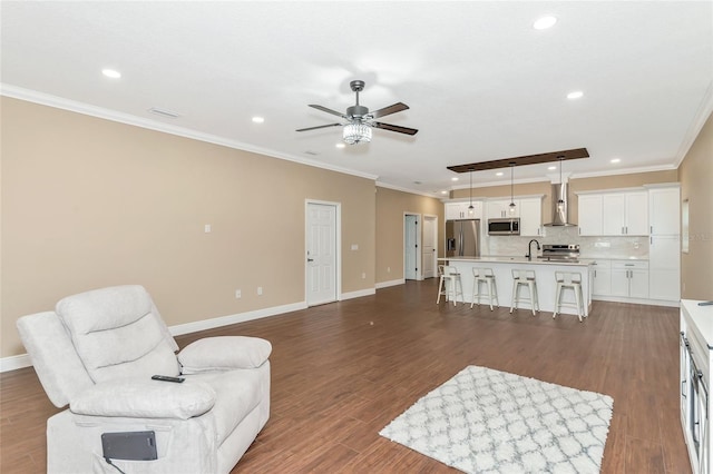 living room featuring ceiling fan, sink, ornamental molding, and dark wood-type flooring