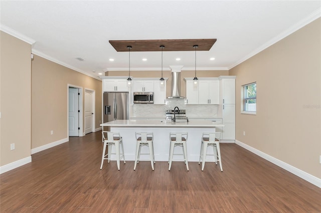 kitchen featuring dark wood-type flooring, stainless steel appliances, wall chimney range hood, pendant lighting, and a kitchen island with sink