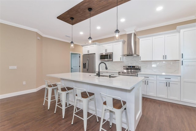 kitchen with wall chimney range hood, sink, decorative light fixtures, white cabinetry, and stainless steel appliances