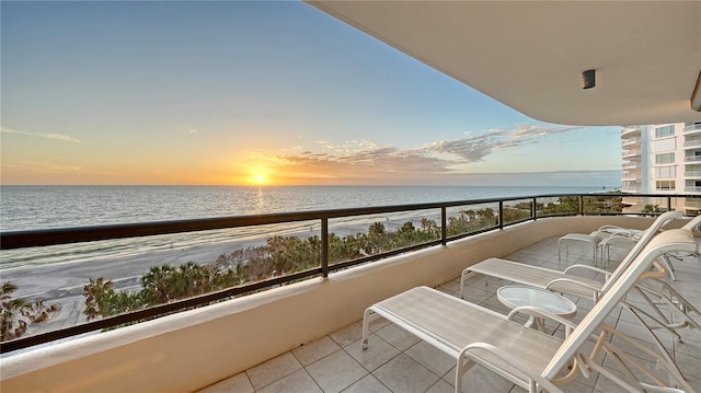 balcony at dusk featuring a water view and a beach view