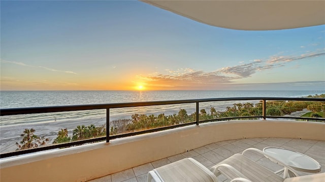 balcony at dusk featuring a water view and a beach view