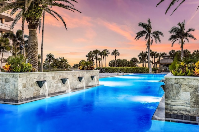 pool at dusk featuring pool water feature