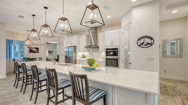 kitchen featuring wall chimney exhaust hood, stainless steel appliances, a spacious island, pendant lighting, and white cabinetry