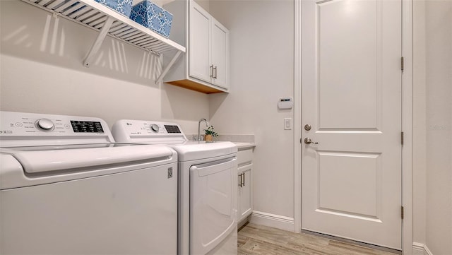 laundry area featuring washer and clothes dryer, cabinets, and light hardwood / wood-style flooring