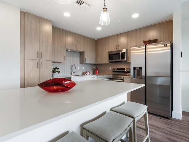 kitchen with sink, stainless steel appliances, backsplash, hardwood / wood-style floors, and pendant lighting