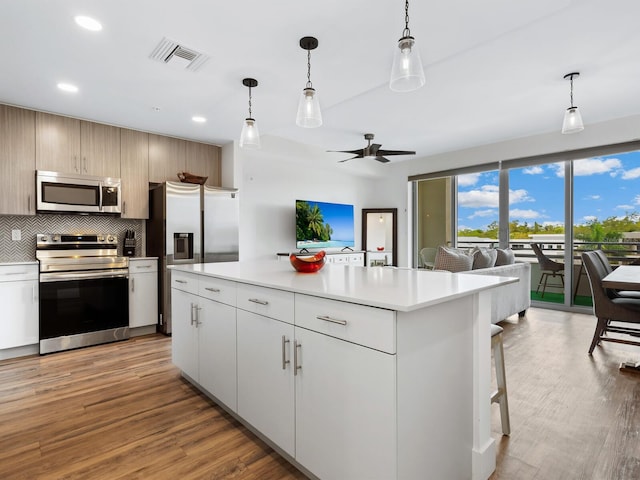 kitchen featuring decorative light fixtures, light hardwood / wood-style floors, a kitchen island, and appliances with stainless steel finishes