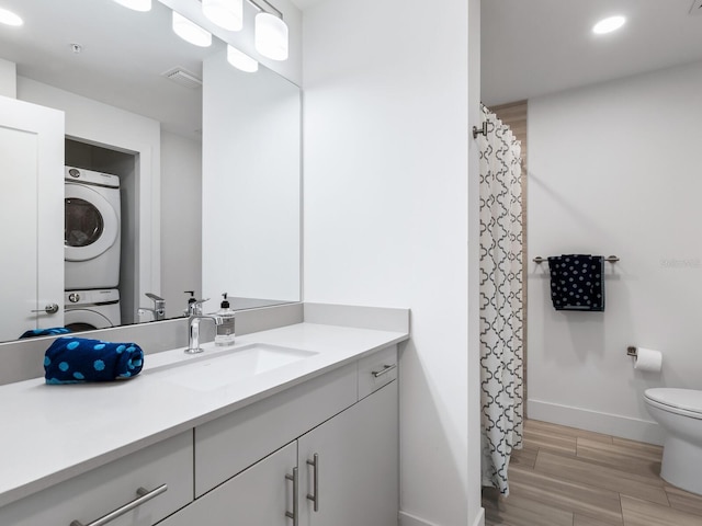 bathroom with hardwood / wood-style floors, vanity, stacked washer / drying machine, and toilet