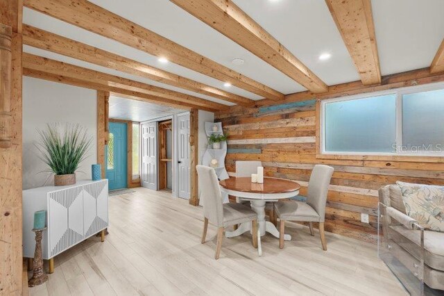 dining room with wood walls, beam ceiling, and light hardwood / wood-style flooring