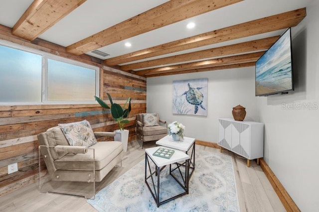 living area with beamed ceiling, wood walls, and light wood-type flooring