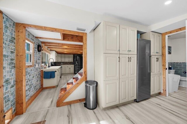 kitchen featuring cream cabinets, black fridge, beamed ceiling, light hardwood / wood-style floors, and stainless steel refrigerator