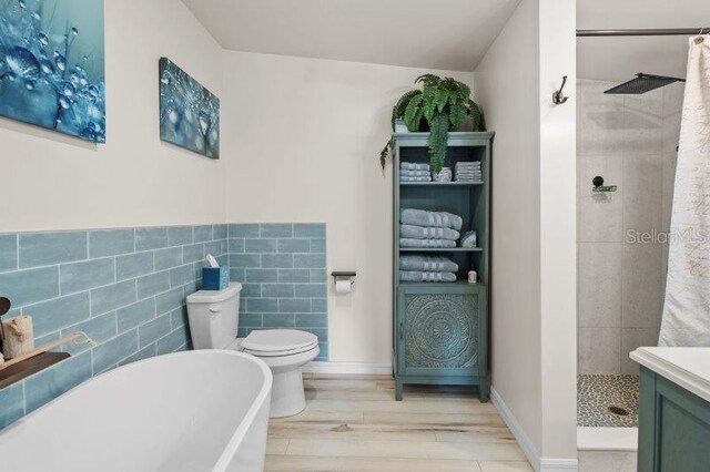 full bathroom featuring shower with separate bathtub, hardwood / wood-style floors, toilet, vanity, and tile walls