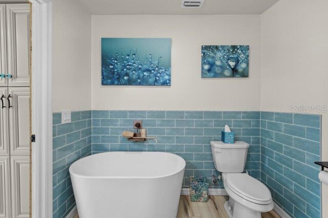 bathroom with a bathtub, toilet, wood-type flooring, and tile walls