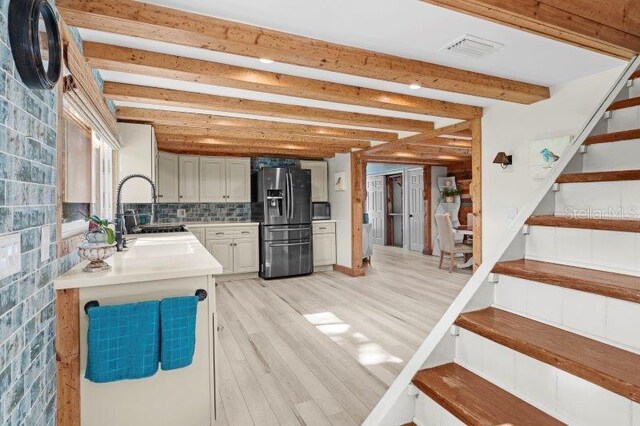 kitchen with sink, decorative backsplash, light wood-type flooring, beamed ceiling, and stainless steel fridge with ice dispenser