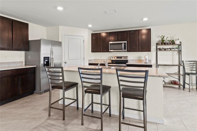 kitchen featuring a kitchen breakfast bar, dark brown cabinetry, stainless steel appliances, and a center island with sink