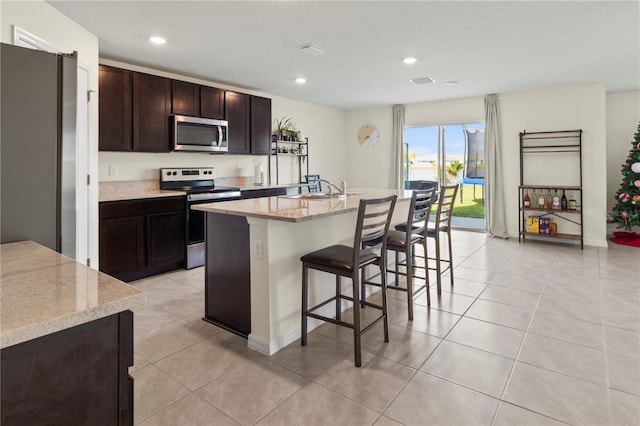 kitchen with light stone counters, sink, an island with sink, and stainless steel appliances