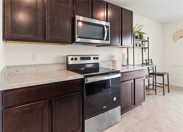 kitchen with light tile patterned flooring, light stone counters, dark brown cabinetry, and stainless steel appliances