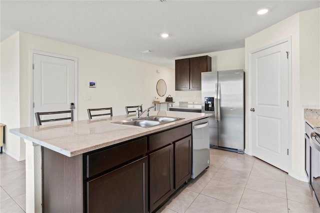 kitchen with a kitchen breakfast bar, dark brown cabinetry, stainless steel appliances, a kitchen island with sink, and sink