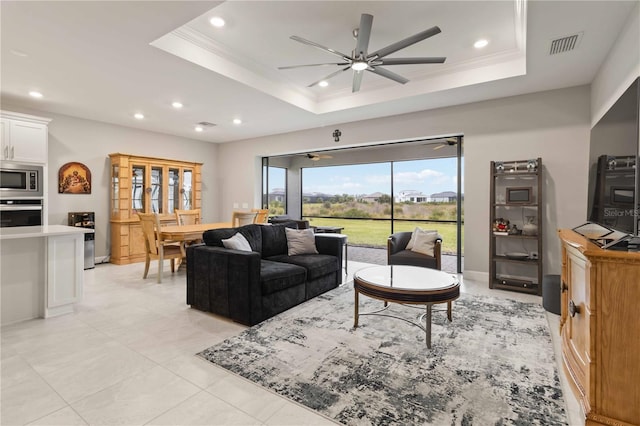 tiled living room featuring ceiling fan, ornamental molding, and a tray ceiling