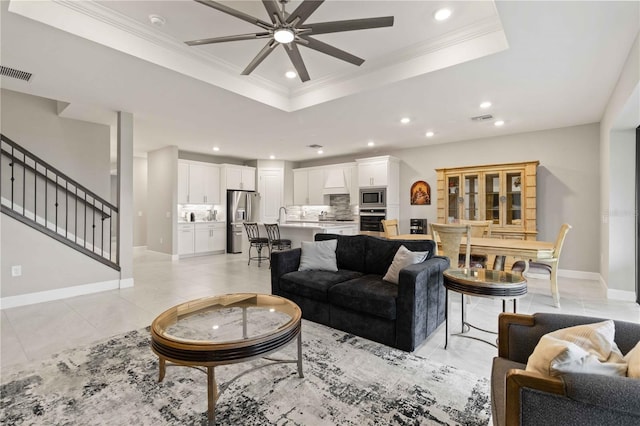 tiled living room featuring a raised ceiling, ceiling fan, ornamental molding, and sink