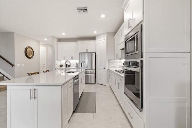 kitchen featuring sink, a kitchen island with sink, stainless steel appliances, decorative backsplash, and white cabinets