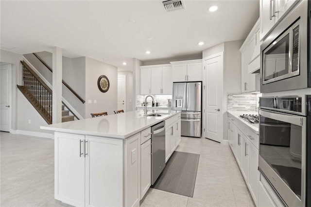 kitchen with a center island with sink, white cabinets, sink, decorative backsplash, and stainless steel appliances