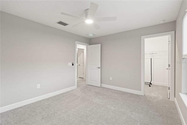 unfurnished bedroom with a closet, light colored carpet, a spacious closet, and ceiling fan