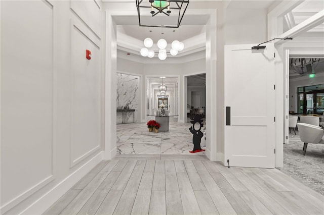 corridor featuring a tray ceiling, light hardwood / wood-style flooring, a notable chandelier, and crown molding