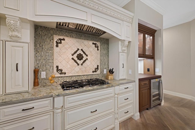 kitchen with beverage cooler, stainless steel gas cooktop, crown molding, decorative backsplash, and light wood-type flooring