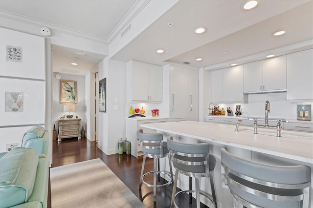 kitchen featuring dark hardwood / wood-style floors, light stone countertops, ornamental molding, a kitchen bar, and white cabinetry