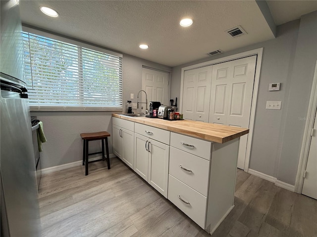 kitchen with butcher block countertops, light hardwood / wood-style floors, white cabinets, and sink