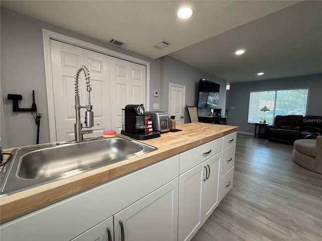 kitchen featuring wooden counters, a textured ceiling, sink, light hardwood / wood-style flooring, and white cabinetry