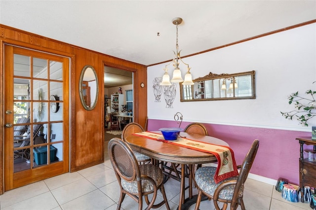 tiled dining area featuring wood walls, crown molding, and an inviting chandelier