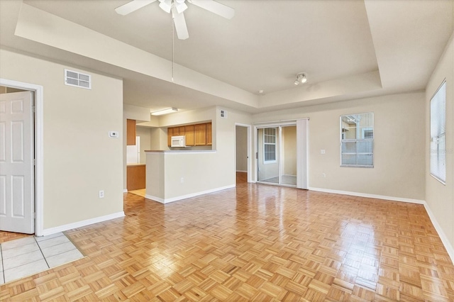 unfurnished living room with a tray ceiling, ceiling fan, and light parquet floors