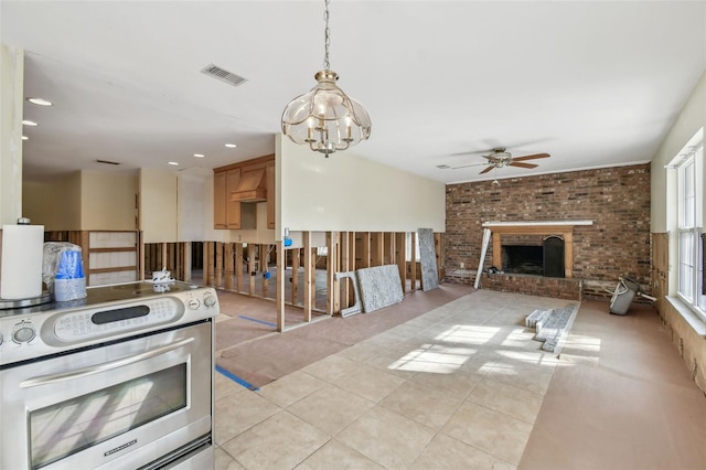 kitchen featuring stainless steel electric stove, ceiling fan with notable chandelier, a fireplace, and brick wall