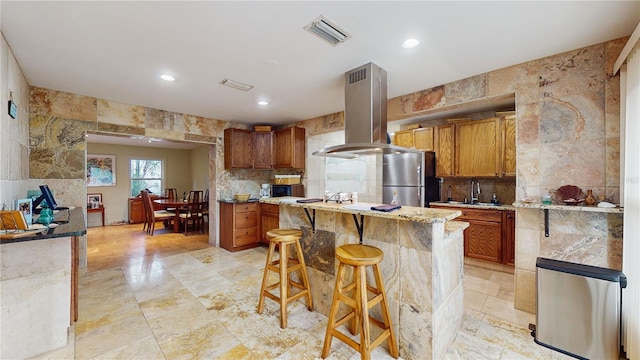 kitchen featuring a breakfast bar, a center island, island range hood, light stone counters, and stainless steel appliances